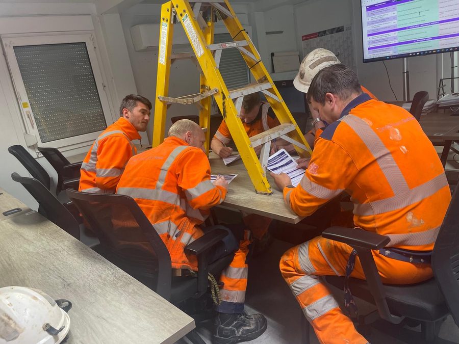 A group of workers in hi-vis completing ladder inspection paperwork around a step ladder during a training session